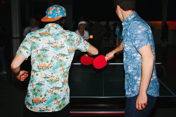 Two players tapping red paddles together across an indoor PingPong table.