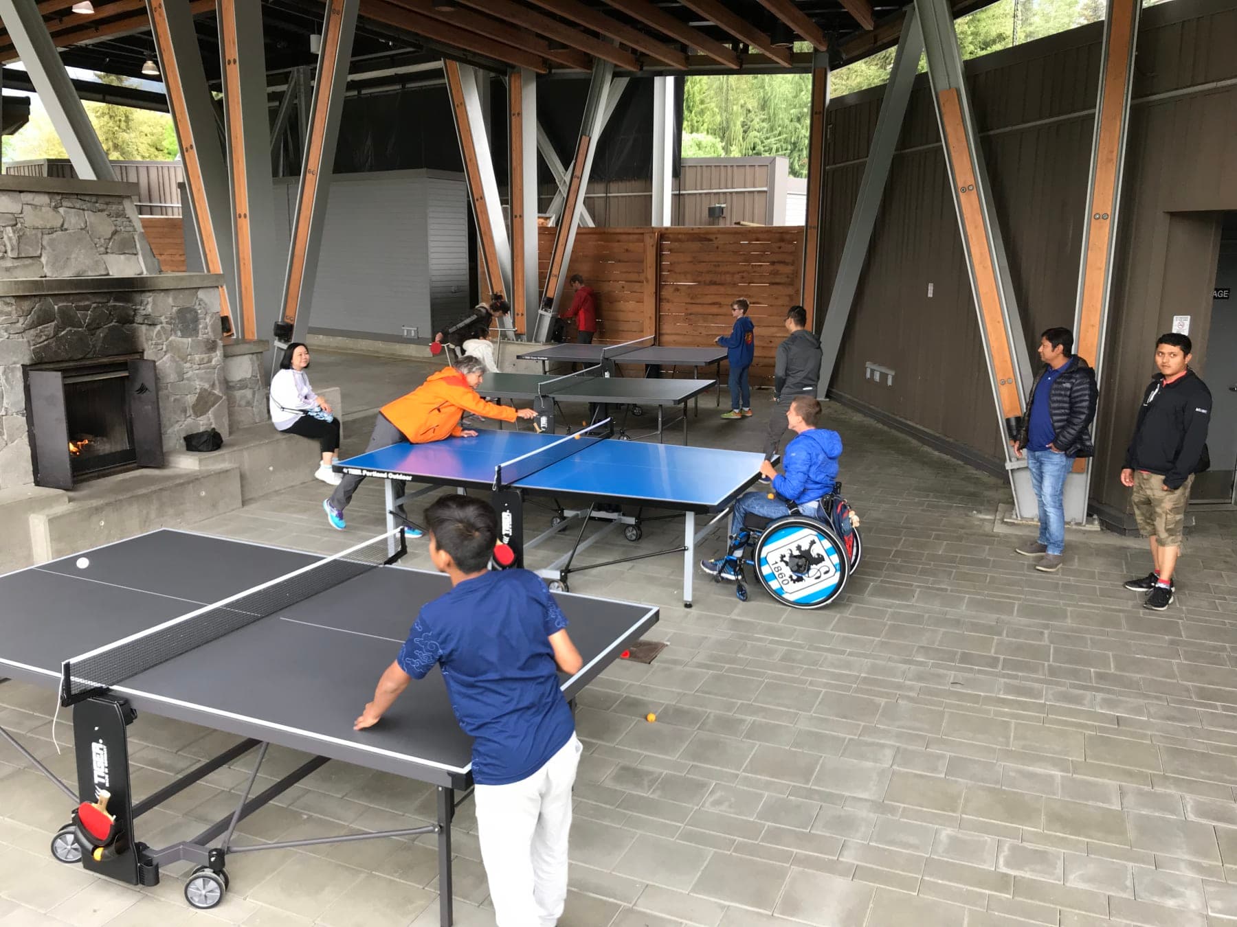 People playing on several Tiger tables at an open-air Whistler pavilion, including a player using a wheelchair.