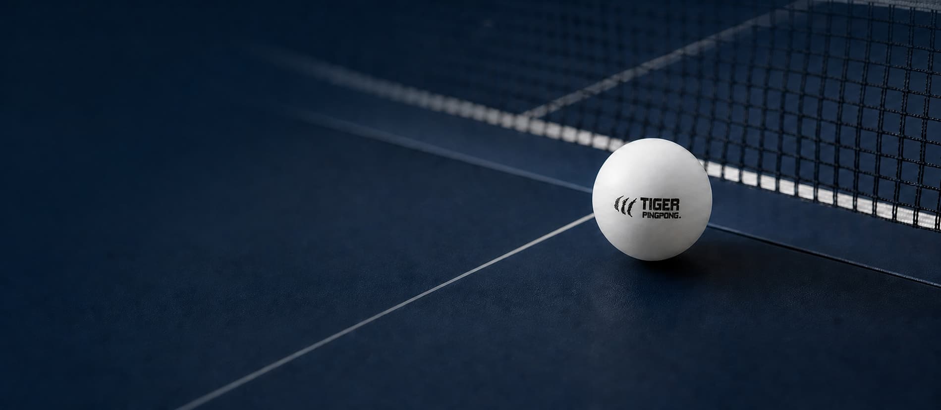 White PingPong ball with the black Tiger scratches and wordmark beside a net on a deep navy table.