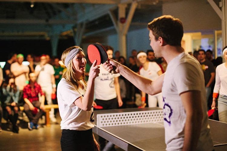 Two players smiling and tapping paddles after a game in a crowded Vancouver venue.