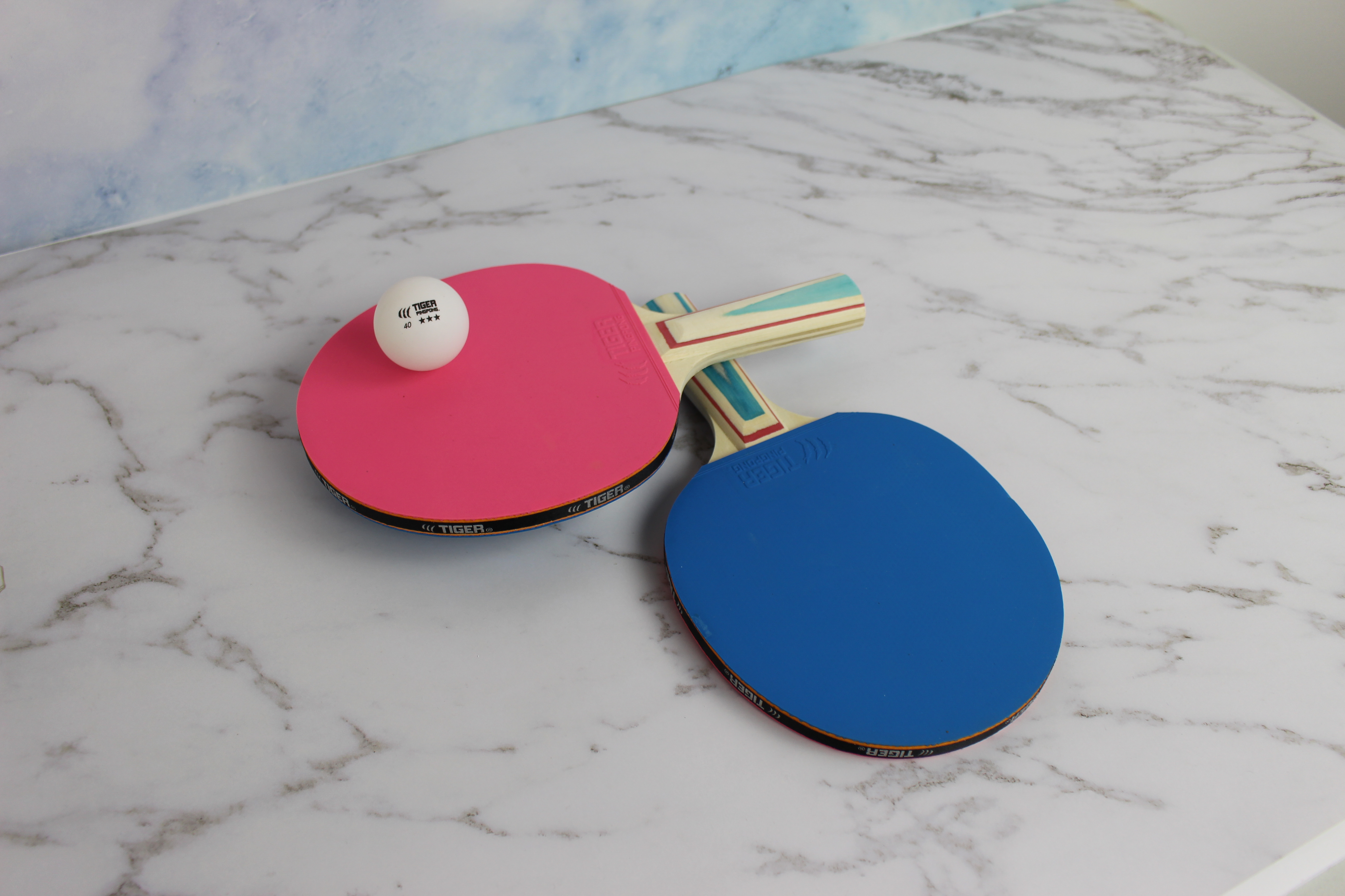 Ping pong ball on top of two ping pong paddles that are lying on a marble counter
