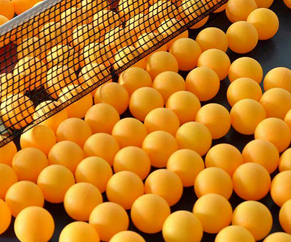 Orange ping pong balls on a table tennis table with a net.